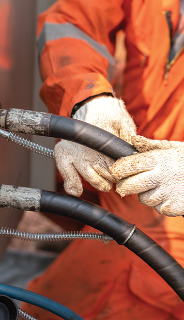 worker in orange coveralls using gloves to handle industrial hoses and cables for machinery maintenance